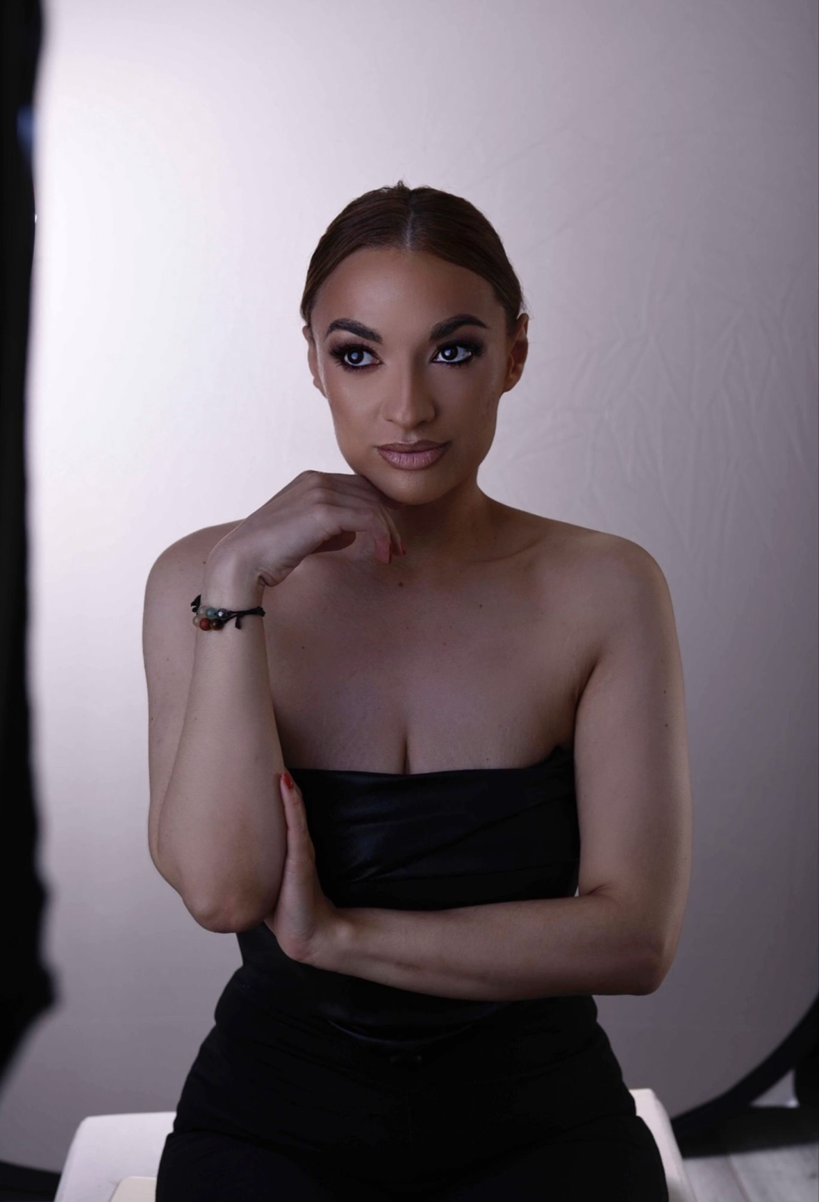 Three quarter modelling shot of Chantelle facing forward sat down on a bench wearing simple black outfit. 